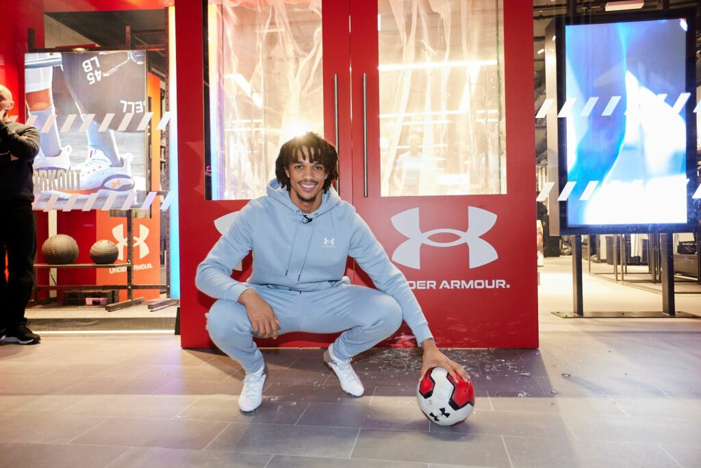 footballer trent alexander arnold crouches in front of the under armour store holding a ball