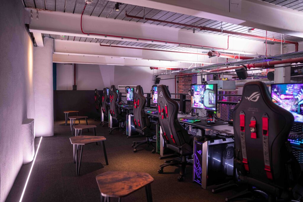 An image showing a row of gaming chairs and screens in a dark lit bar