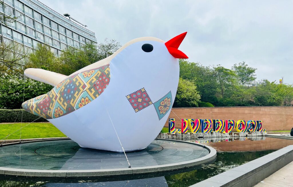 a huge bird installation on a shallow pool in front of a backdrop of trees