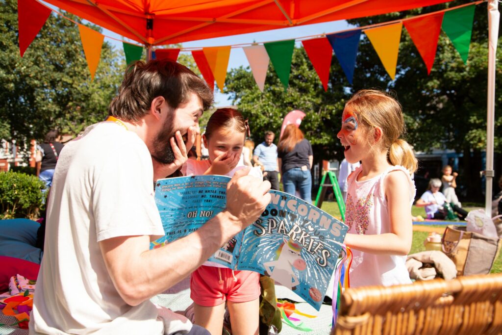 An adult reading a story book to two children in a park