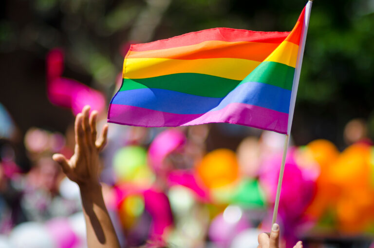 Hand waving in front of rainbow flag during pride parade